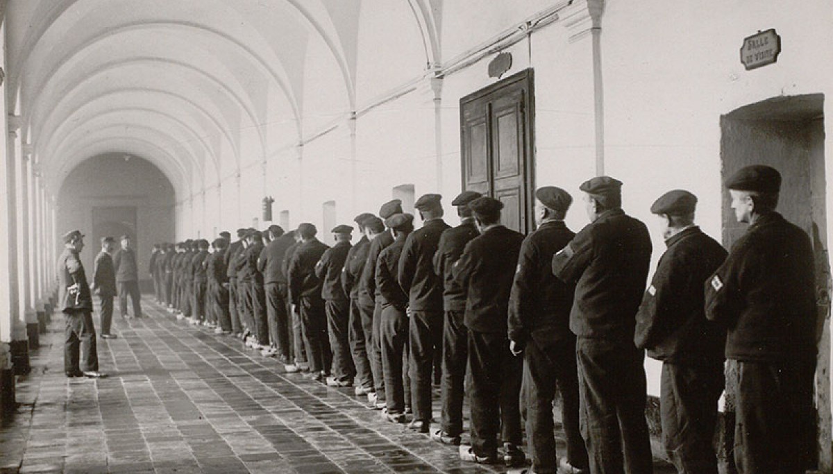 Maison centrale de Nîmes : détenus au prétoire, 1932 – Photographie d’Henri Manuel (Coll. Enap-Crhcp), On notera le numéro d’écrou cousu sur la manche de la veste.